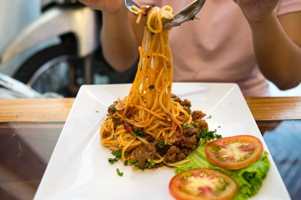 Женщина ест спагетти с мясом на белом квадратном блюде — стоковое фото