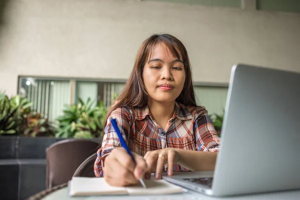 Mujer asiática trabajando en portátil y escribiendo cuaderno en la cafetería — Foto de Stock