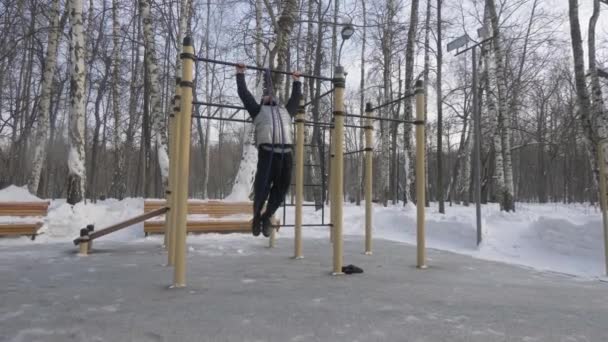 Hombre joven entrenamiento tire de ejercicio en el travesaño durante el entrenamiento al aire libre — Vídeos de Stock