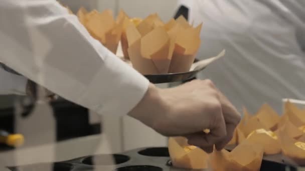 Руки пекаря положить на поднос кексы в бумажной обертке в пекарне — стоковое видео