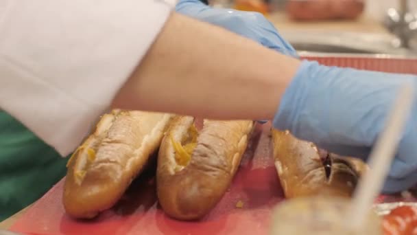 Handen cook stukken worst aanbrengend knippen van stokbrood in fast-food café — Stockvideo