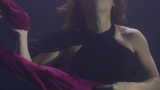 Mysterious woman in chiffon dress swimming underwater pool on dark background. — Stock Video