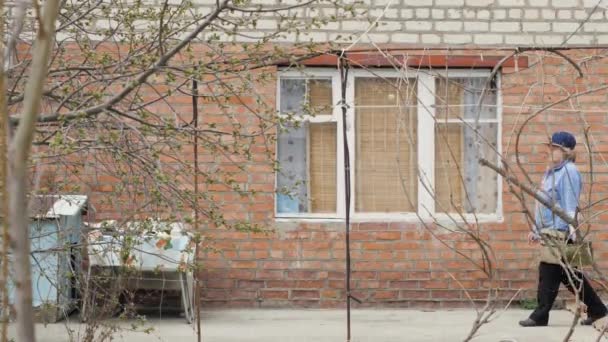 Стара жінка садівник з водяним горщиком, що йде на фоні будівлі перерви — стокове відео