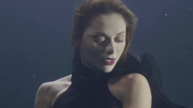 Portre sualtı yüzme koyu arka plan üzerinde siyah elbiseli güzel kadın