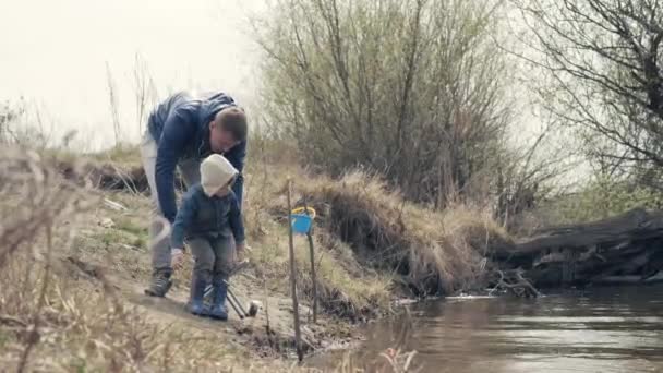 Padre e hijo pescando juntos en el río. Niño pequeño con caña de pescar en la orilla — Vídeo de stock