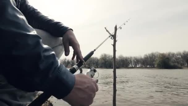 Manos pescador girando carrete de pesca en la caña durante la picadura de peces en el agua del río — Vídeo de stock