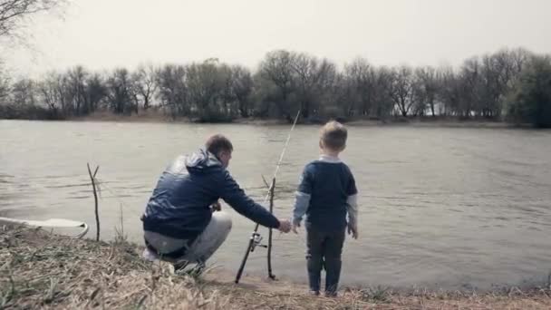 Молодой отец и маленький сын рыбачат вместе в речной воде — стоковое видео