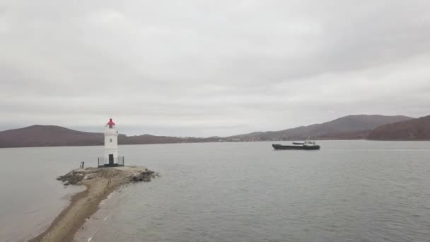 Cargo ship floating in sea and lighthouse on sea shore view from flying drone — Stock Video