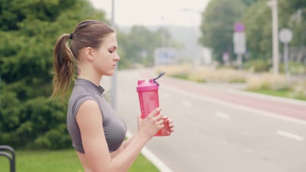 Γυμναστήριο γυναίκα πόσιμο νερό από το μπουκάλι ενώ υπαίθρια αθλητική προπόνηση — Αρχείο Βίντεο