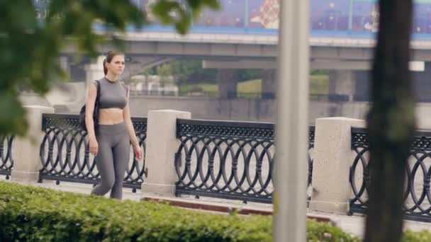 Jovem mulher em sportswear e saco de fitness andando no parque de verão — Vídeo de Stock