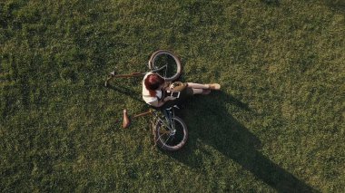 Yeşil çim üzerinde yalan ve cep telefonuyla dron görünümü kadın bisikletçi