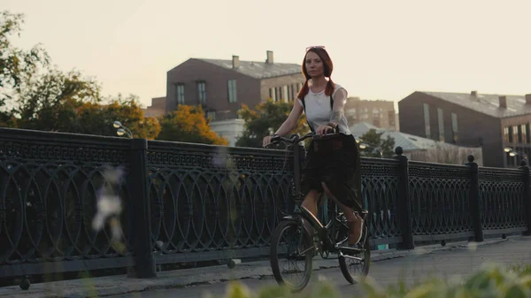 Red haired woman riding bicycle in city on background facade building