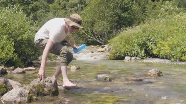 Törstig man tar flaska vatten från fjällbäck och dricka på camping — Stockvideo