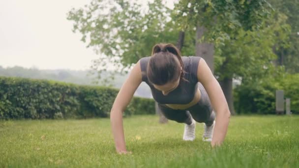 Fitness tjej gör push ups övningar under utomhus träning i sommar park — Stockvideo