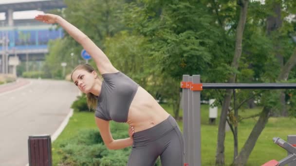 Chica joven haciendo ejercicios de calentamiento y estiramiento en el gimnasio de entrenamiento al aire libre — Vídeos de Stock