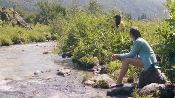 坐在河的石岸上的年轻妇女和休息在夏天天 — 图库视频影像
