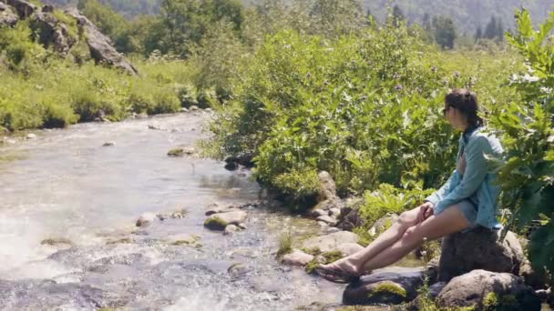 Femme touristique reposant sur la rive de la rivière et regardant sur l'eau courante — Video