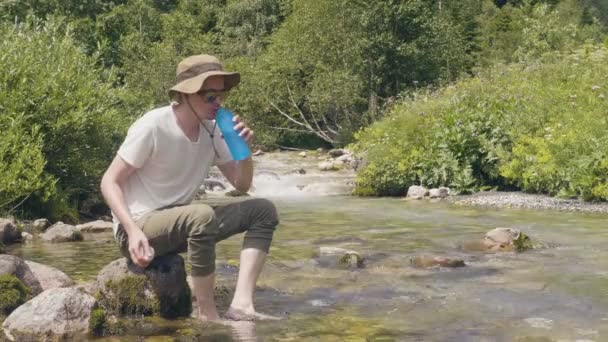 Muž vezme láhev vody z horské řeky na letní lezení na cestách — Stock video