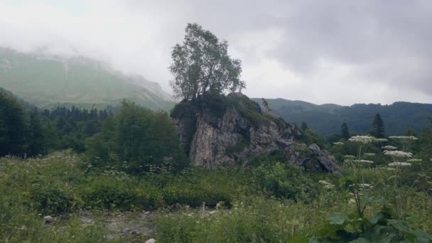 Turistické lidí lezení na skalnatém útesu na zelené horské krajiny, zatímco pěší turistika — Stock video