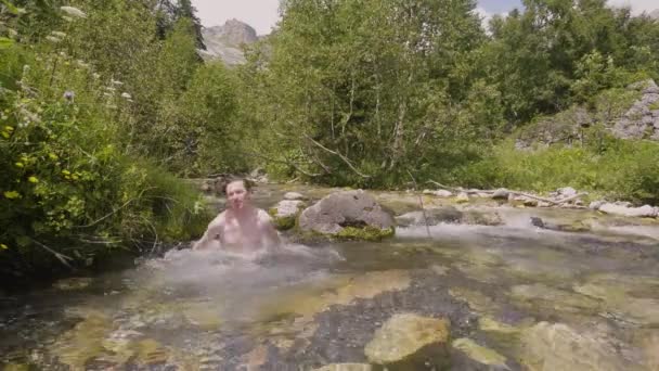 Молодой человек купается в воде горной реки в жаркий летний день — стоковое видео