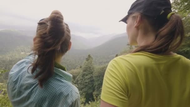 Δύο γυναίκα στέκεται στην κορυφή του βουνού και κοιτάζοντας σε πράσινους λόφους και τα δάση — Αρχείο Βίντεο