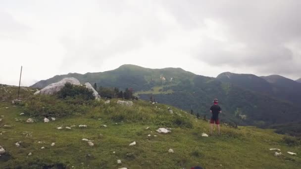 Homme debout sur le bord du sommet de la montagne sur fond vert vallée drone vue — Video