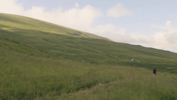 Randonneur homme marchant sur le champ vert sur fond de montagnes et de collines — Video
