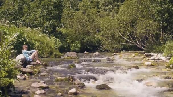 Erholsame Frau am steinigen Flussufer während einer Sommerwanderung. Wilde Naturlandschaft — Stockvideo