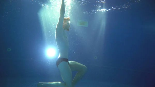 Un joven da saltos mortales y hace un salto mortal bajo el agua. Está posando delante de la cámara. Vista submarina . —  Fotos de Stock