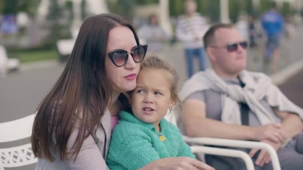 Ung mamma hålla lilla dotter i sommar park, far sitter nära å — Stockvideo