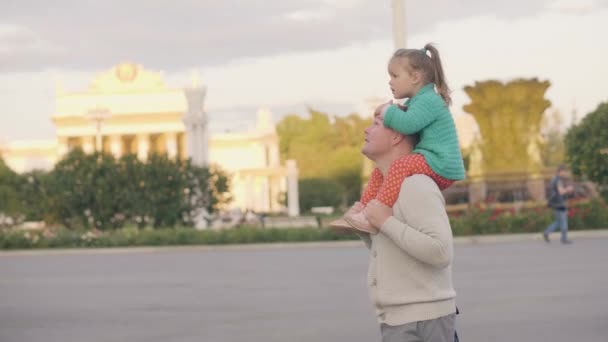 Söt liten dotter rider på axlar far vandrar i sommar stadsparken — Stockvideo