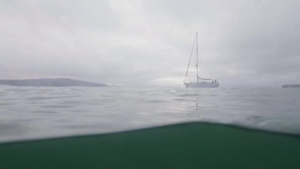 Підводний вигляд яхта з білим вітрилом, що пливе в морі. Стрілянина під час підводного плавання — стокове відео