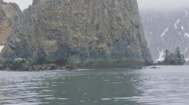 Kayalık ada ve yelkenli gemi deniz panoramik görünümü içinde karlı dağlar