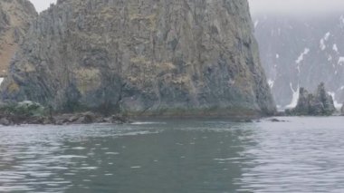 Kayalık ada ve yelkenli gemi deniz panoramik görünümü içinde karlı dağlar