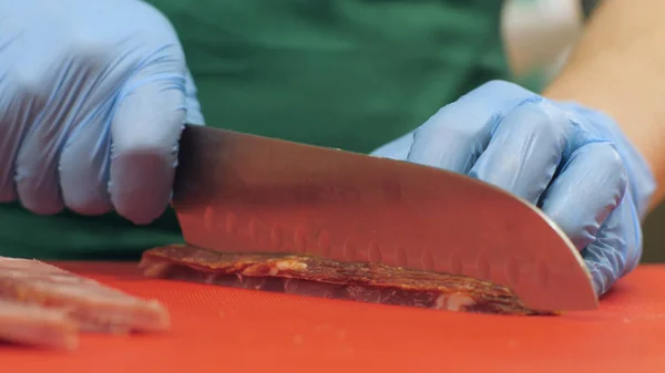 Manos de cocinero usando cuchillo para cortar carne seca mientras cocina en restaurante — Foto de Stock