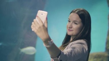 Genç kadın oceanarium arka plan üstünde hareket eden telefon için selfie fotoğraf için poz