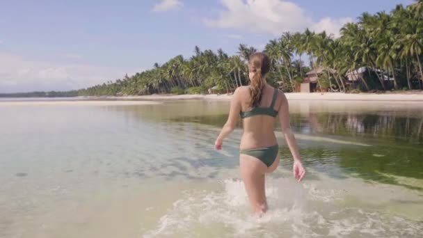 Jonge vrouw in zwembroek lopen op transparante zeewater op tropisch strand. Gelukkige vrouw genieten van helder water op oceaan eiland. Zomervakantie op paradijs strand. — Stockvideo