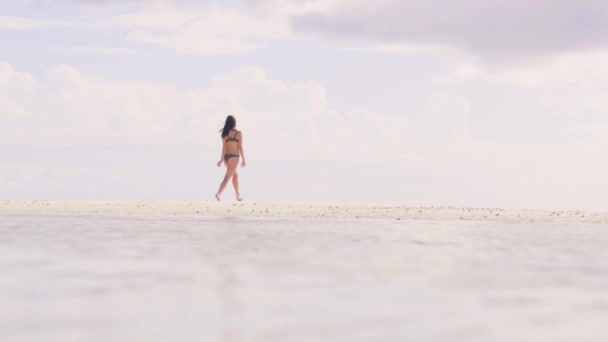Jonge vrouw in strand bikini springen en dansen op wit zand. Gelukkige vrouw genieten van zomerdag op zanderige eiland en zee water achtergrond. Lage hoek schieten vrolijk meisje op oceaan strand. — Stockvideo