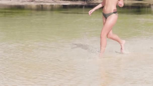 Mulher despreocupada em maiô correndo na água na praia do mar. Mulher sorridente desfrutando de água do mar na praia de verão no fundo verde palmeiras na costa. Menina feliz posando na ilha do paraíso . — Vídeo de Stock