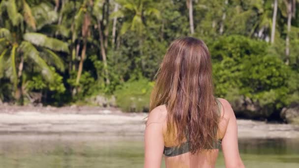 Portrét bruneta žena dotýká mokré vlasy a pózuje pro kameru na pláži moře. Usmívající se žena na tropické pláži v zelené palm tree pozadí. Veselá dívka si letní dovolenou na exotický ostrov. — Stock video