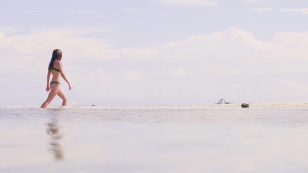 Νεαρή γυναίκα στο μπικίνι περπάτημα στο νερό της θάλασσας, στην αμμώδη παραλία στον παράδεισο θέρετρο. Χαμηλή γωνία προβολής. Όμορφη γυναίκα που τρέχει στο νερό των ωκεανών στην παραλία το καλοκαίρι. Καλοκαιρινές διακοπές. — Αρχείο Βίντεο