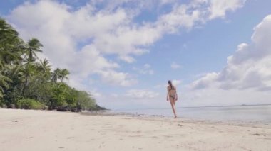Bikini üzerinde yürüyen genç kadın kum gökyüzü sahilde deniz üzerinde bir palmiye ağaç görünümü ıslak. Güzel kız mayo okyanus plaj yaz günü zevk. Düşük açılı görünüş