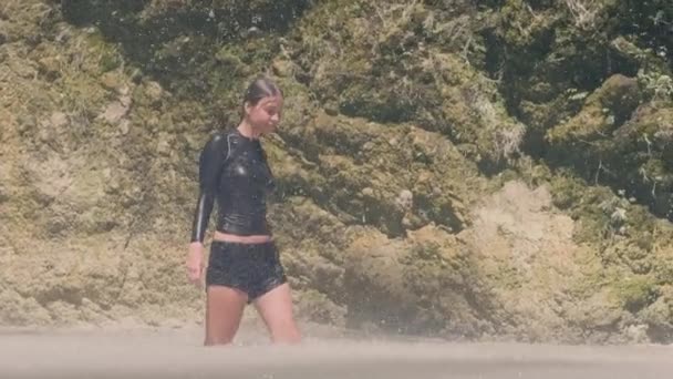 Femme insouciante en vêtements humides profitant de gouttes d'eau tombant de la cascade de montagne dans la jungle. Fille attirante dans un lac de montagne sous l'eau coulant de fali d'eau tropicale dans la forêt tropicale . — Video