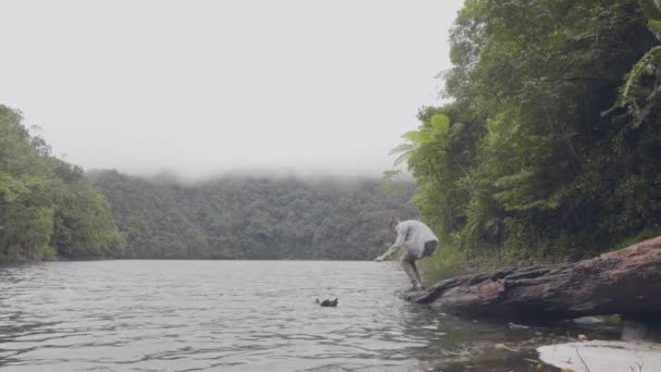 관광 남자 열 대 강 흐르는 녹색 언덕 사이에서 손을 씻는 정글을 덮여 있다. 여행자 남자 강 물에 빠지는 및 열 대 고원의 풍경에 손을 씻는 나무에 앉아. — 비디오
