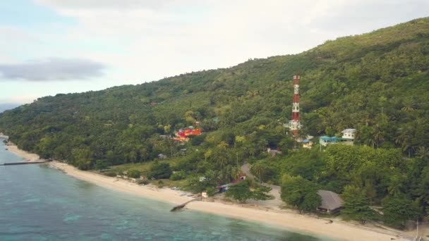 Vista aérea de la torre de comunicaciones y la construcción de tierras altas verdes en la orilla del mar. Casas vista Drone y edificios en la colina verde en la orilla tropical del océano . — Vídeo de stock