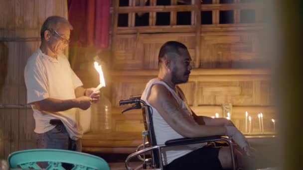 Curandeiro queimando vela durante ritual mágico para o tratamento homem doente em cadeira de rodas em casa mágica. Tradicional asiático ritual de cura. Tradições étnicas autênticas . — Vídeo de Stock