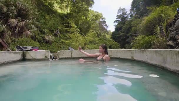 Giovane donna che fa il bagno termale facendo foto selfie al telefono cellulare. Donna beauty blogger utilizzando smartphone per selfie mobili in bagno minerale. Terme naturali e terapia del corpo . — Video Stock