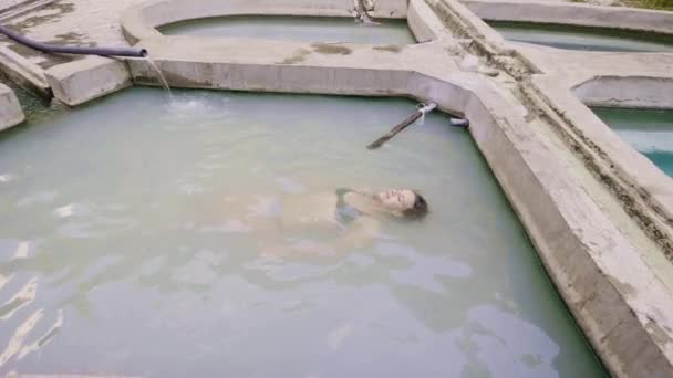 Mulher relaxante nadando na piscina de água mineral no resort spa ao ar livre. Mulher feliz desfrutando de banho termal da primavera natural. Terapia de spa e relaxamento . — Vídeo de Stock