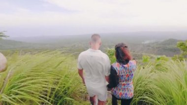 Mutlu bir çift güzel manzara ile yeşil dağ kenarında yürüyüş. Genç adam ve kadının inanılmaz yüksek dağ yataydan tropikal orman kaplı.