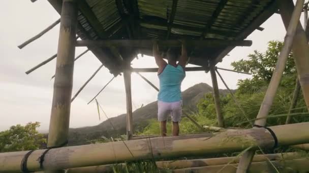 Junger Mann trainiert Bauchmuskeln am Querbalken vor tropischem Hintergrund. Athlet Mann beim Bauchtraining am Reck während des Outdoor-Fitnessstudios. — Stockvideo